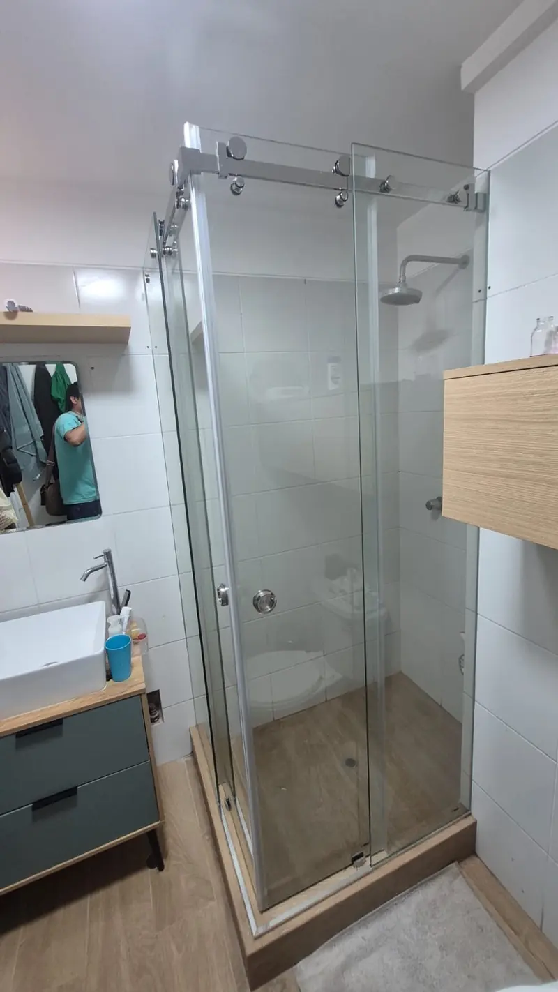 Cabina de ducha en vidrio templado con herrajes de acero inoxidable en baño moderno